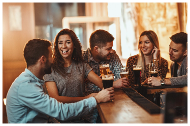 three men and two woman sit around a wooden table enjoying themselves while drinks various colours of beer