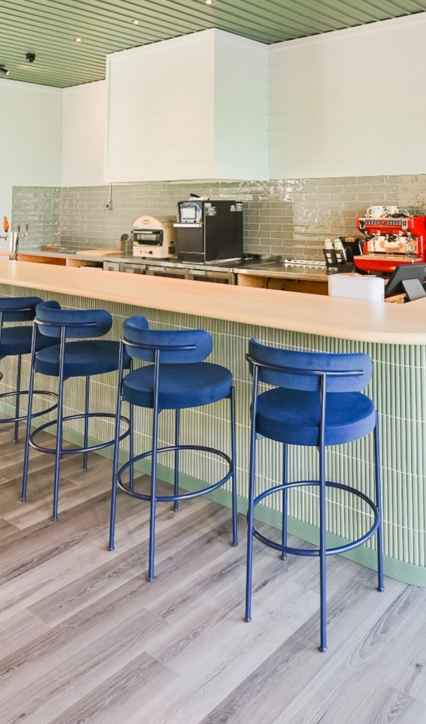 a bright bar area with blue stools with seat backs and coffee machines on the counter behind the bar